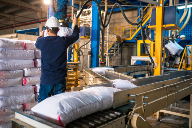 Photo of a worker loading Rows or stacks of white sack bags at large warehouse in modern factory.